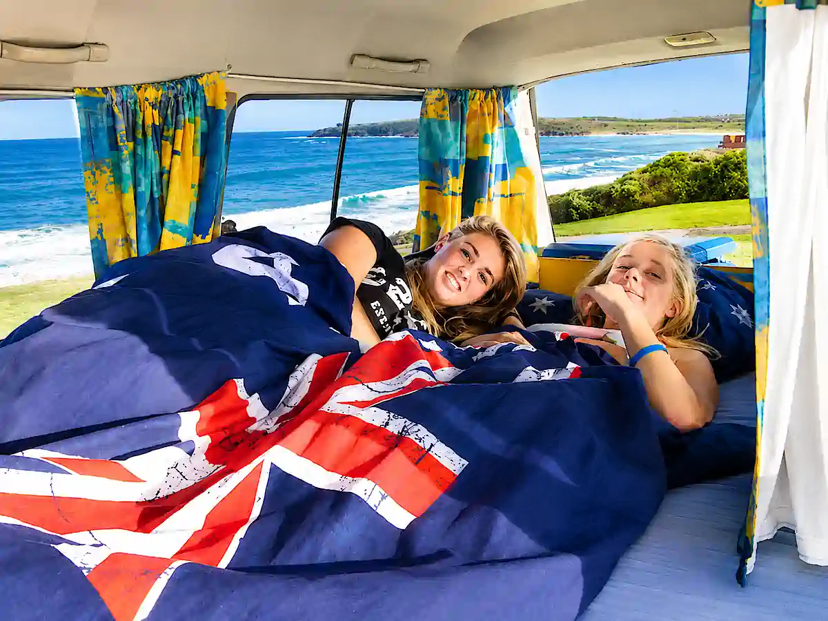 Backpacker Camper in Sydney kaufen – zwei Reisende im Doppelbett mit Meerblick
